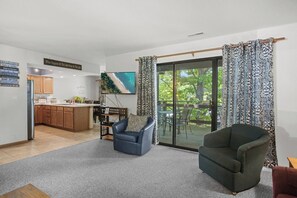 Een woonkamer met een bank, een stoel, een televisie en een schuifdeur naar een terras.