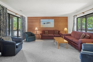 A living room with a wooden wall, a painting, and a view through large windows.