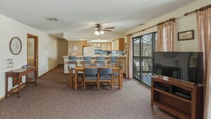 A hotel room with a dining area, a TV, a ceiling fan, and a large window.