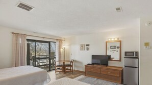 A hotel room with two beds, a television, a refrigerator, a dining table with chairs, and a balcony with a view.
