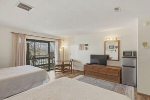 Ein Hotelzimmer mit zwei Betten, einem Fernseher, einem Kühlschrank, einem Esstisch mit Stühlen und einem Balkon mit Blick.
