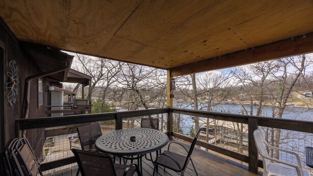 A wooden deck with a round table and chairs, overlooking a body of water.