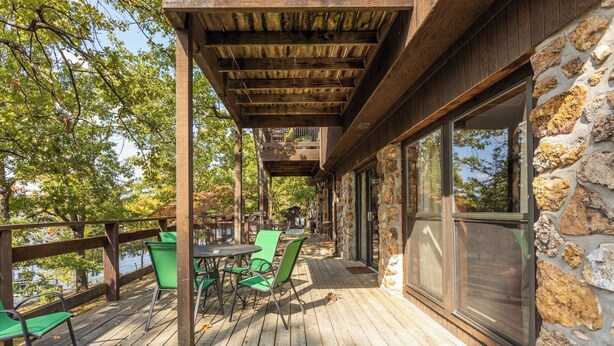 A wooden deck with outdoor seating, a stone wall, and a view of trees.