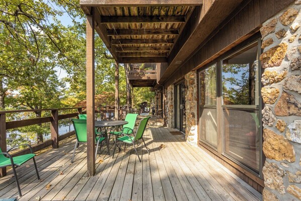 A wooden deck with outdoor seating, a stone wall, and a view of trees.