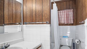 A bathroom with wooden cabinets, a white sink, a toilet, and a shower curtain.