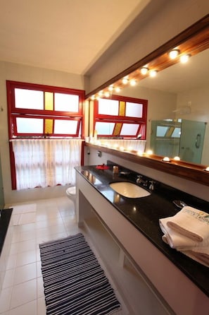 A bathroom with a large mirror, a sink, and a window with curtains. - Pousada Mar de Dentro (Florianópolis)