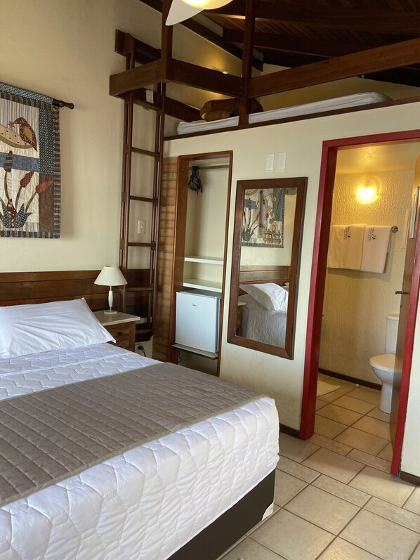 Une chambre à coucher comprenant un lit, un bureau, un réfrigérateur, un miroir et une salle de bain visible à travers une porte ouverte.
