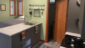 Une cuisine de taille réduite, équipée d’un évier, d’une cuisinière et d’une fenêtre donnant sur les arbres.