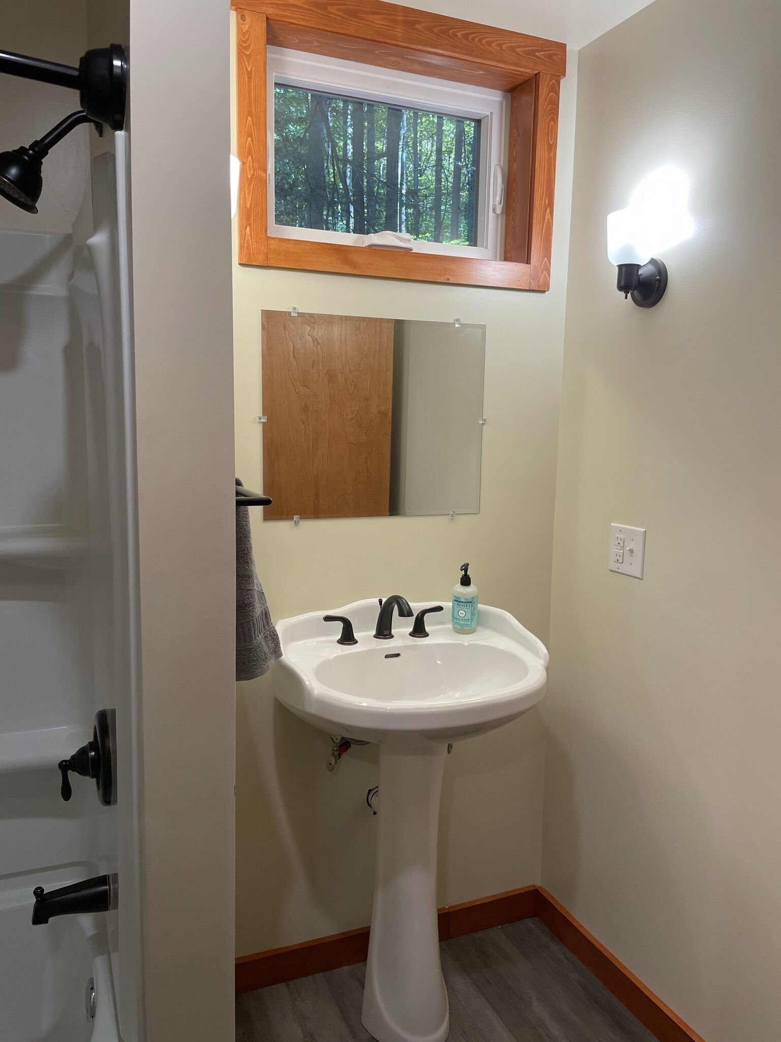 A bathroom with a white sink, a mirror, a window with a view of trees, and a towel hanging on the wall.