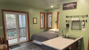 Une chambre compacte comprenant un lit, une petite kitchenette et une porte-fenêtre coulissante donnant sur un balcon.