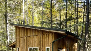 Une cabane en bois dotée d’un porche couvert et d’une allée en gravier, entourée d’arbres.