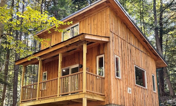 A wooden cabin with a balcony, surrounded by trees.