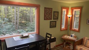 Un coin repas avec une table et des chaises, un petit canapé et une fenêtre donnant sur une forêt.