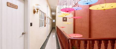 A hotel hallway with a wooden railing, a nameplate on a door, and hanging umbrellas.