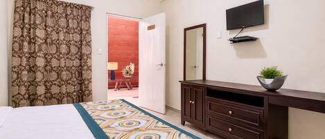 A bedroom with a bed, a dresser, a television, and a door leading to a red-walled room.