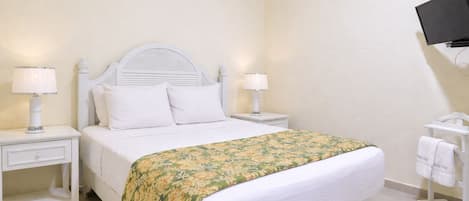 Quarto de hotel bem arrumado, com uma cama, duas mesas de cabeceira com luminárias, uma TV fixada na parede e um porta-toalhas.