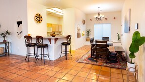 Una cocina amplia con una isla central, un comedor con una mesa grande y sillas, y una sala de estar con una araña.