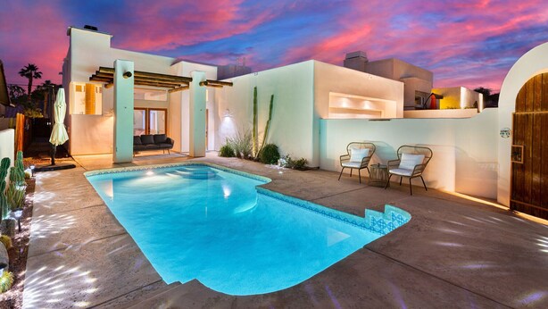 Una casa moderna con piscina, un patio con sillas y un cielo al atardecer.