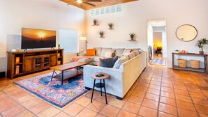 Sala de estar con sofá, mesa de centro, televisor, techo de madera y plantas en macetas.