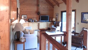Interior acogedor de una cabaña con techo de madera, un sofá, un sillón, un televisor y una mesita con una lámpara.