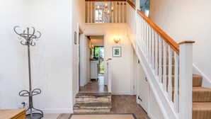 Un escalier avec des rampes en bois et un lustre, menant à une pièce dotée d’une porte et d’un tableau encadré au mur.