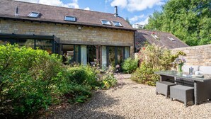 Une maison en pierre avec une allée en gravier, un espace extérieur aménagé pour s’asseoir et un jardin.