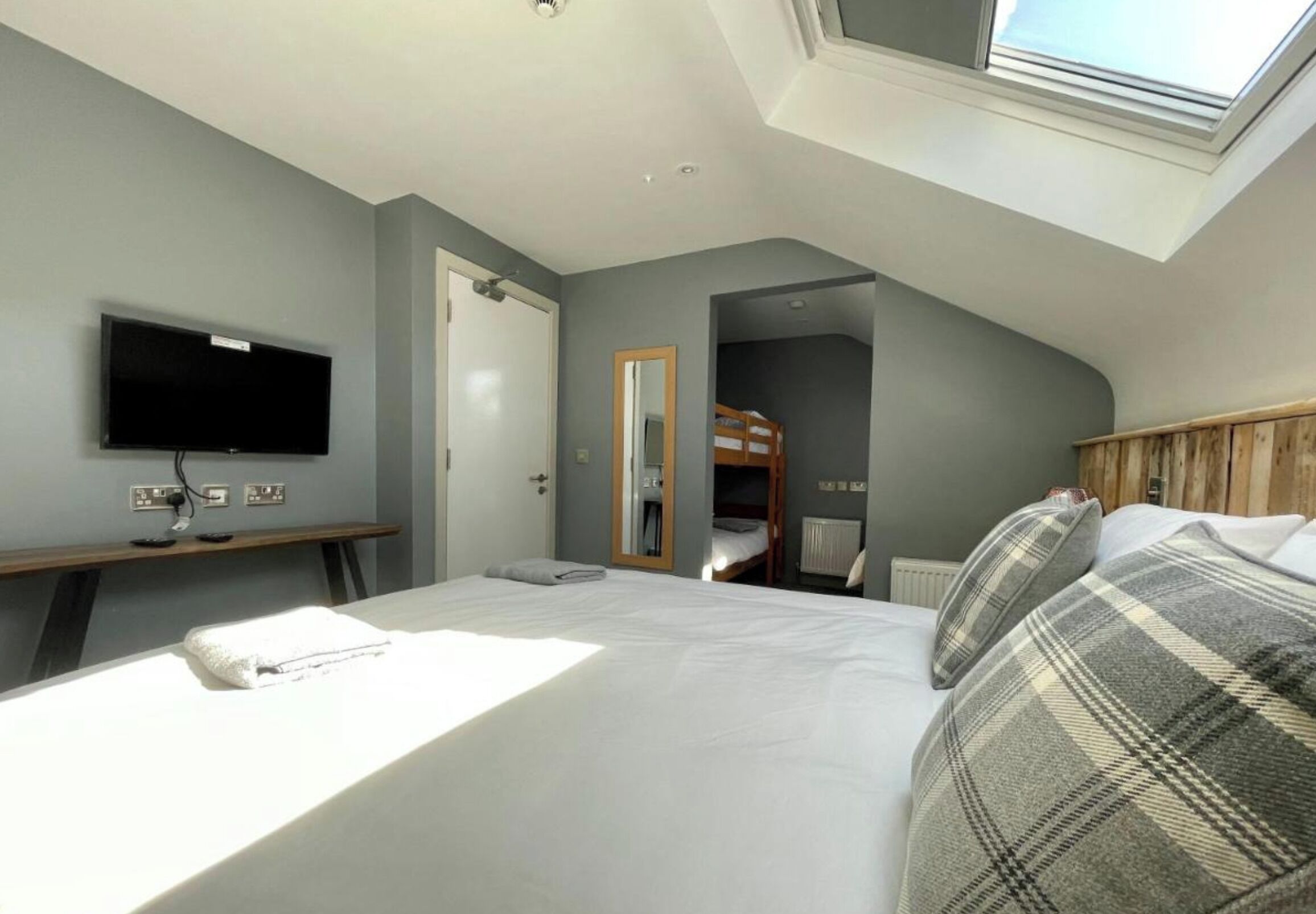 A bedroom with a bed, a television, a skylight, and a bunk bed in the corner.