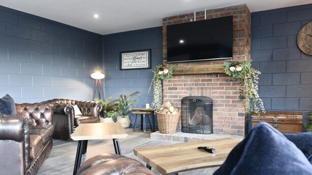 A cozy living room with a brick fireplace, leather sofa, and a flat-screen TV mounted above it. - Rostrevor Mountain Lodge (Newry)