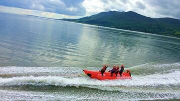 A group of people on a red watercraft moving across a calm lake with mountains in the background.