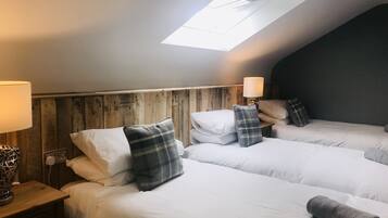 Une chambre d’hôtel avec trois lits, des têtes de lit en bois et une lucarne.