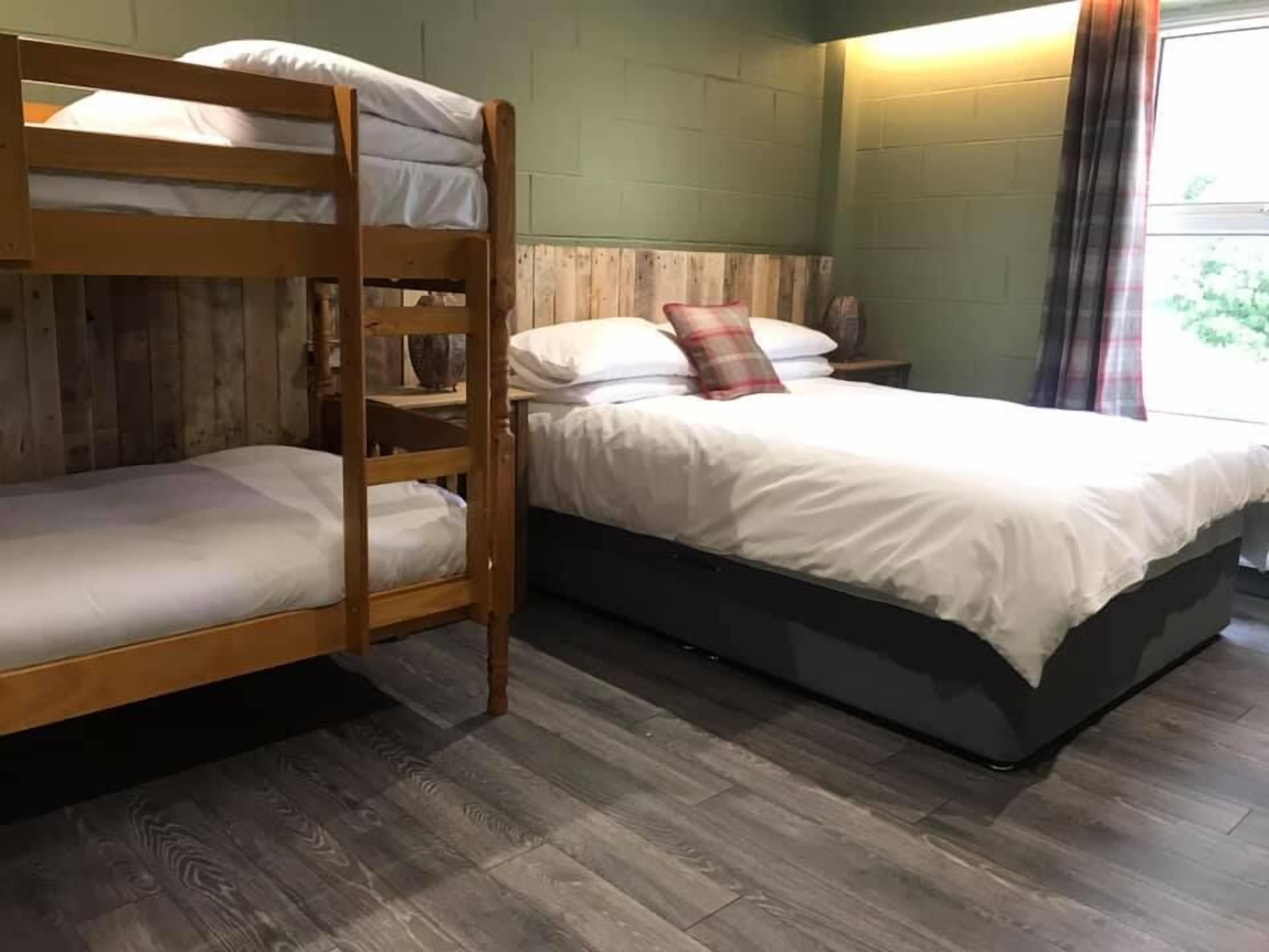 Quarto com beliche, chão de madeira, mesa de cabeceira e janela com cortinas.