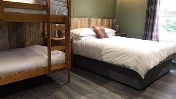 Quarto com beliche, chão de madeira, mesa de cabeceira e janela com cortinas.