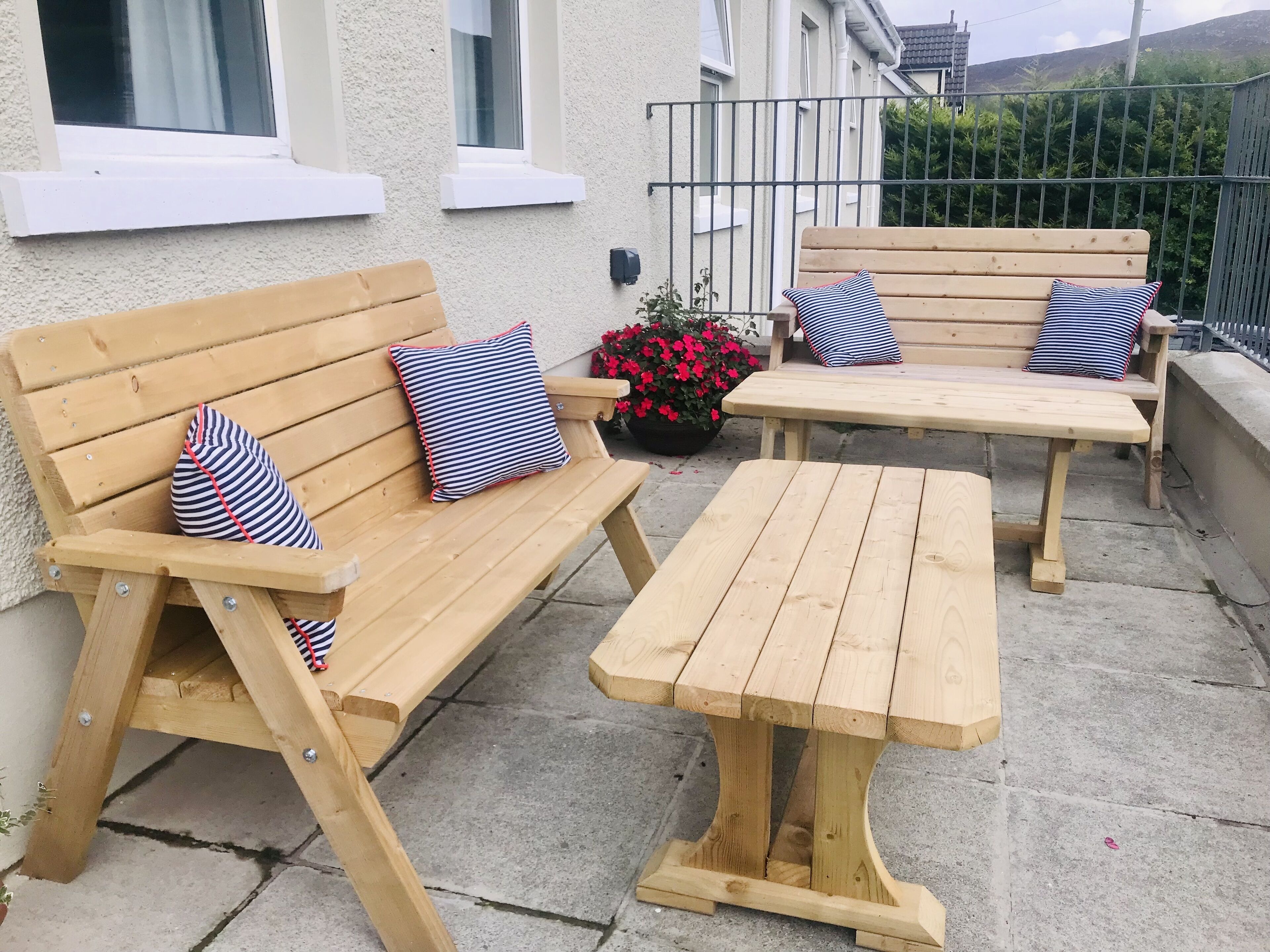 A wooden outdoor seating area with benches and a table, surrounded by a low wall and a window.