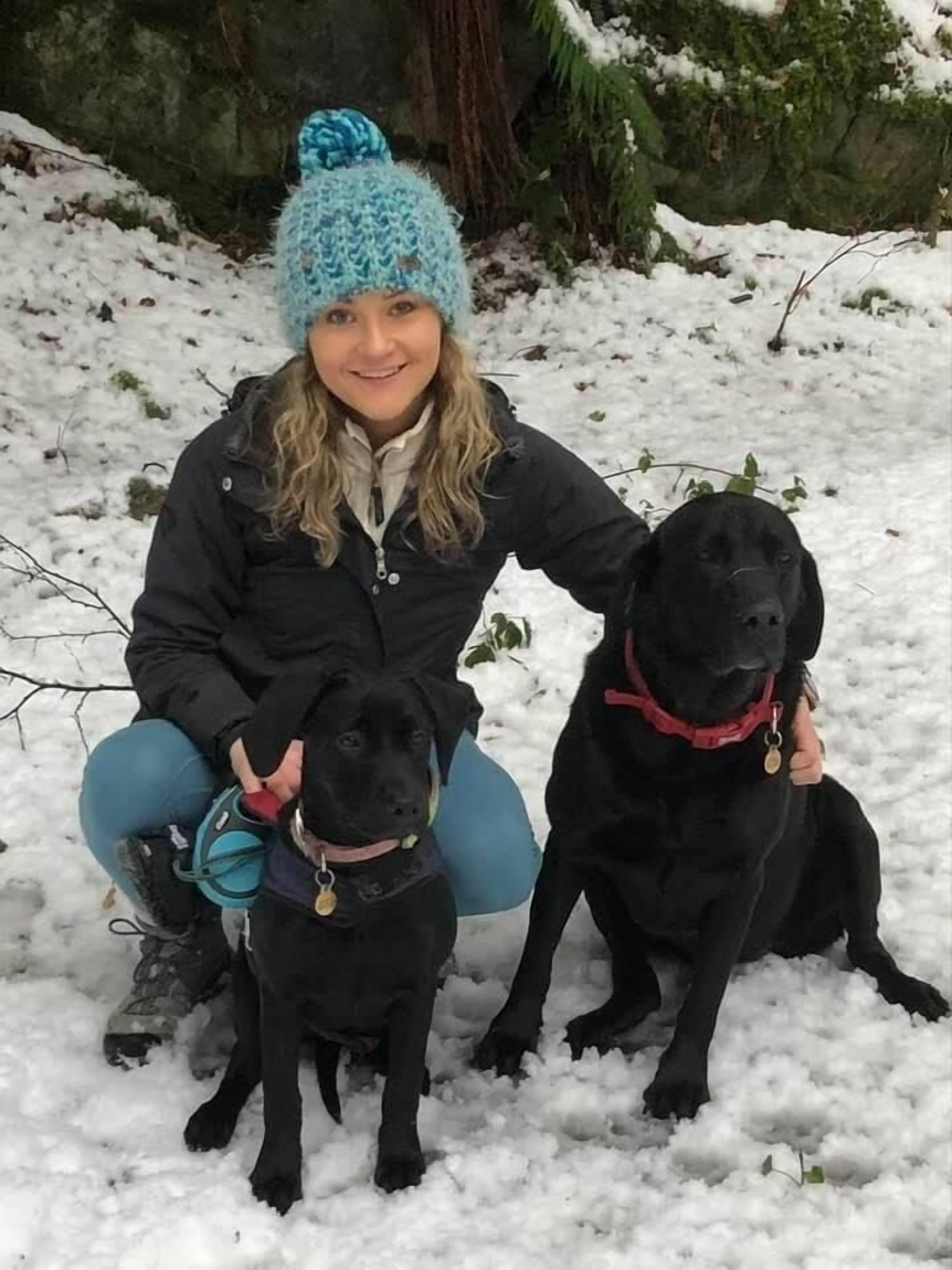 Une personne assise par terre, accompagnée de deux chiens, dans un décor extérieur enneigé.