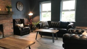 A living room with a brick fireplace, leather sofas, a wooden coffee table, and large windows. - Rostrevor Mountain Lodge (Newry)