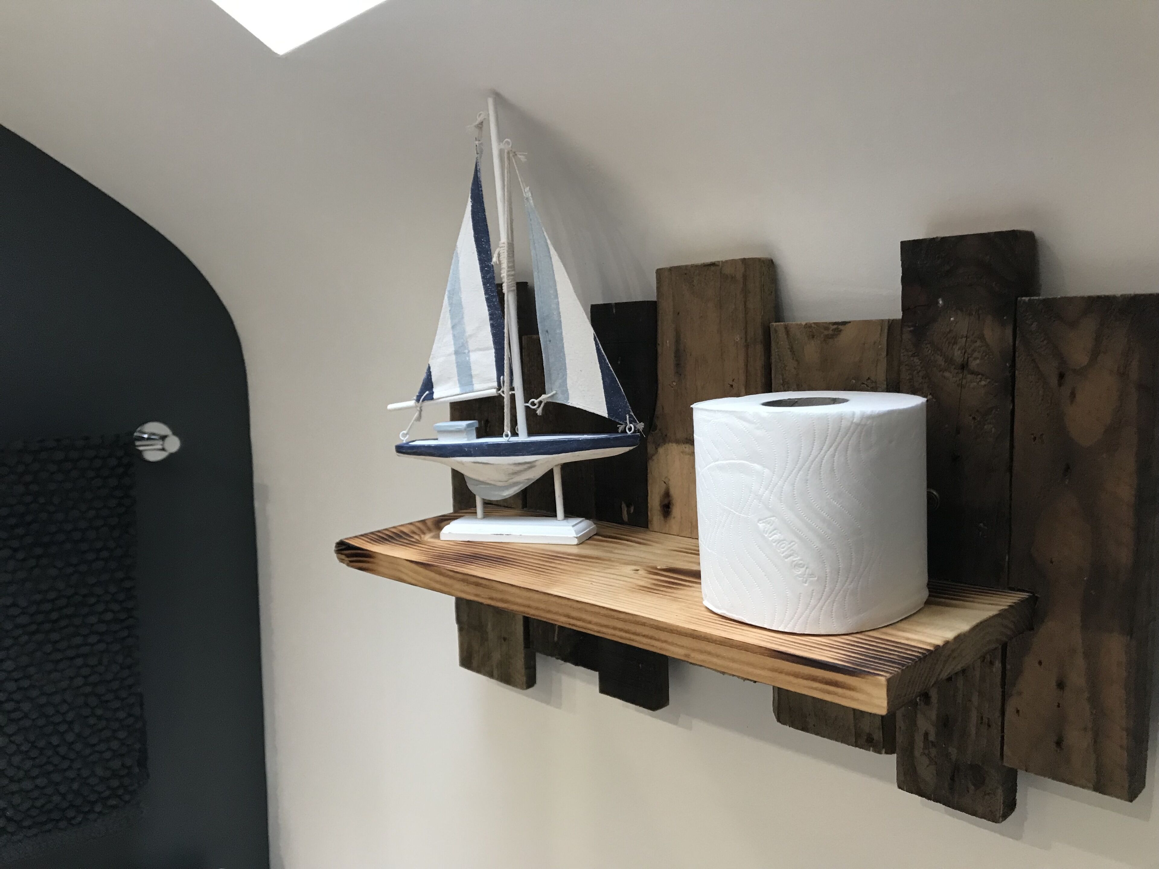 A wooden shelf with a sailboat model and a roll of toilet paper.