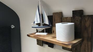 A wooden shelf with a sailboat model and a roll of toilet paper.