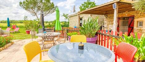 A patio with a round glass table and chairs, surrounded by potted plants and a stone building.