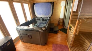Une cabane en bois avec un jacuzzi, un plancher en bois et une porte en verre.