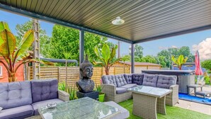Une terrasse extérieure aménagée avec des meubles en osier, une statue de Bouddha et un jacuzzi.