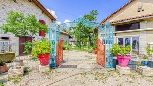 Une entrée de village rustique, agrémentée d’une porte décorative, de bâtiments en pierre et de plantes en pot.