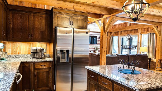 A kitchen with wooden cabinets, a stainless steel refrigerator, granite countertops, and a hanging light fixture. - Dreams Park/All Star- Sunset Lodge at Old World Village (Maryland)