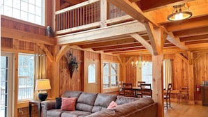 A spacious wooden cabin interior with a high ceiling, a cozy living area with a leather sofa, a dining table, and a chandelier. - Dreams Park/All Star- Sunset Lodge at Old World Village (Maryland)