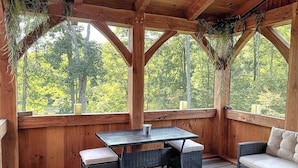 A wooden deck with a table and chairs, surrounded by large windows offering a view of a forest. - Dreams Park/All Star- Sunset Lodge at Old World Village (Maryland)