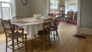 Un comedor con una mesa redonda, sillas de madera, un mantel blanco y un cuenco blanco grande.