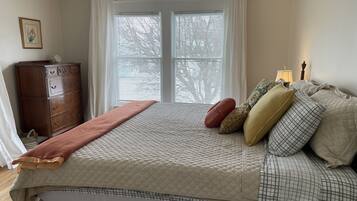 A bedroom with a bed, a dresser, a window with blinds, and a bedside lamp.