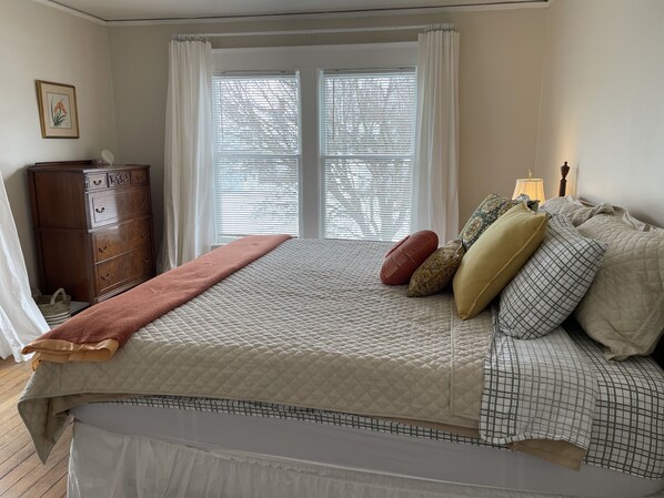 A bedroom with a bed, a dresser, a window with blinds, and a bedside lamp.