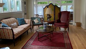 Amplia sala de estar con piso de madera, alfombra roja estampada, un sofá, un sillón, una mesa de centro y una lámpara decorativa.