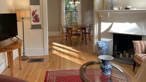 Una sala de estar con televisor, un sofá de cuero rojo, una mesa de centro de vidrio y una chimenea.