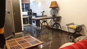 A compact living space with a kitchenette, a dining area with a table and stools, a sofa, and a decorative lamp.